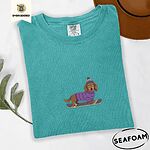 Seafoam Comfort Colors T-shirt embroidered with a long-haired dachshund in a purple sweater and pom-pom beanie riding a snowboard