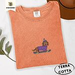 Terracotta Comfort Colors T-shirt embroidered with a long-haired dachshund in a purple sweater and pom-pom beanie riding a snowboard