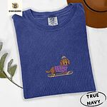 True Navy Comfort Colors T-shirt embroidered with a long-haired dachshund in a purple sweater and pom-pom beanie riding a snowboard