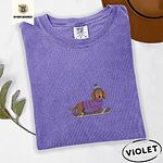 Violet Comfort Colors T-shirt embroidered with a long-haired dachshund in a purple sweater and pom-pom beanie riding a snowboard