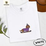 White Comfort Colors T-shirt embroidered with a long-haired dachshund in a purple sweater and pom-pom beanie riding a snowboard