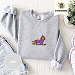Ash crewneck sweatshirt folded with denim shorts, white sneakers and a potted plant, embroidered with a long-haired dachshund in a purple sweater and pom-pom beanie riding a snowboard