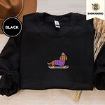 Black crewneck sweatshirt with a brown felt hat and dried bunny tail grass, embroidered with a long-haired dachshund in a purple sweater and pom-pom beanie riding a snowboard