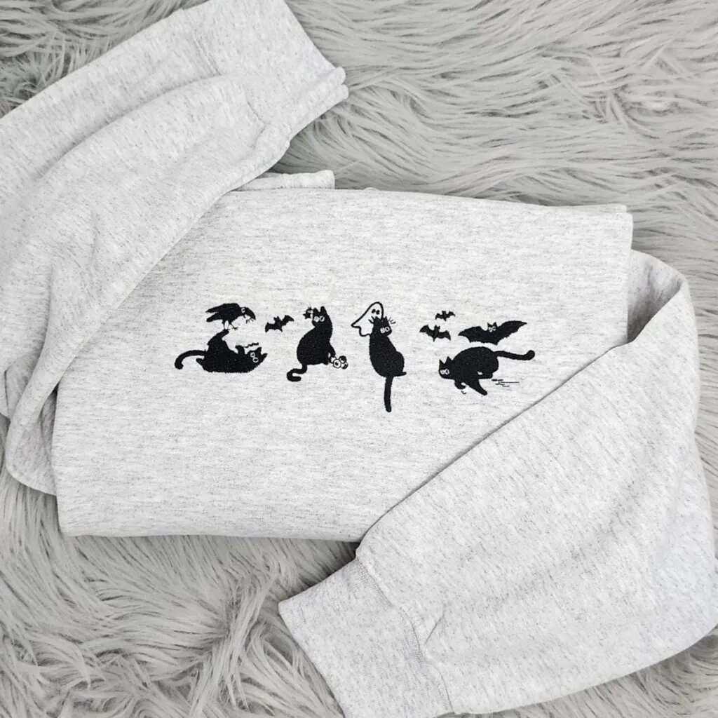 Spooky black cat sweatshirt in light heather grey with four embroidered black cats, a crow, bats and a tiny ghost across the chest
