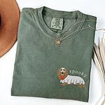 Moss T-shirt laid flat with a necklace and a felt hat, embroidered on the left chest with a long-haired dachshund in a ghost sheet and the word spooky in white