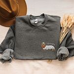 Dark Heather crewneck sweatshirt laid flat with a felt hat and dried wheat, embroidered on the left chest with a long-haired dachshund in a ghost sheet and the word spooky in white
