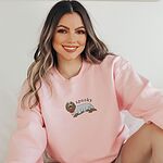 Woman smiling in a Light Pink crewneck sweatshirt embroidered in the center with a long-haired dachshund in a ghost sheet and the word spooky