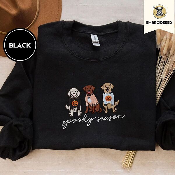 Black crewneck sweatshirt with a brown felt hat and dried bunny tail grass, embroidered with a doodle, a chocolate lab and a golden retriever in Halloween sweaters above spooky season in script