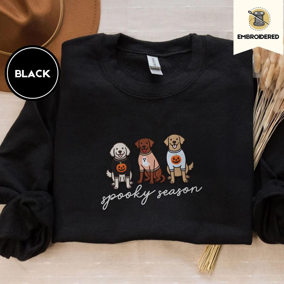 Spooky Pups Sweatshirt – Black Black crewneck sweatshirt with a brown felt hat and dried bunny tail grass, embroidered with a doodle, a chocolate lab and a golden retriever in Halloween sweaters above spooky season in script