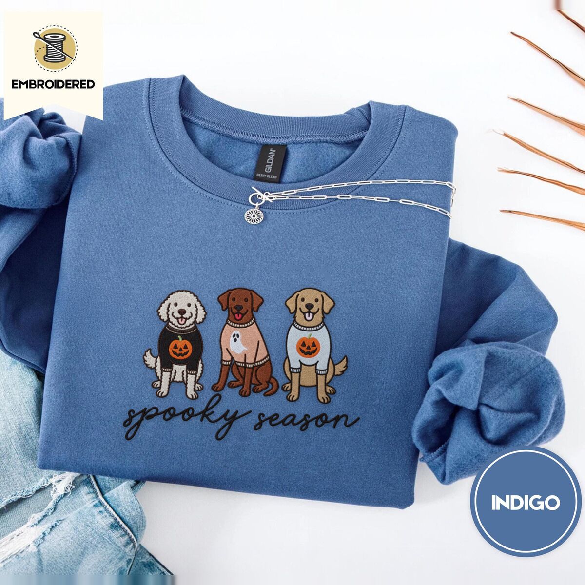 Spooky Pups Sweatshirt – Indigo Blue Indigo Blue crewneck sweatshirt folded with light jeans and dried twigs, embroidered with a doodle, a chocolate lab and a golden retriever in Halloween sweaters above spooky season in script