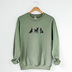 Military Green crewneck sweatshirt hanging on a wooden hanger, embroidered with three black Labradors in a Santa hat and booties, reindeer antlers with a striped scarf, and a Santa hat with a green scarf