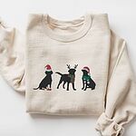 Sand crewneck sweatshirt laid flat with a rolled cuff, embroidered with three black Labradors in a Santa hat and booties, reindeer antlers with a striped scarf, and a Santa hat with a green scarf