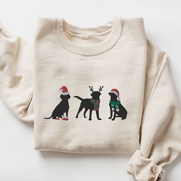 Sand crewneck sweatshirt laid flat with a rolled cuff, embroidered with three black Labradors in a Santa hat and booties, reindeer antlers with a striped scarf, and a Santa hat with a green scarf