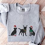 Sport Grey crewneck sweatshirt laid flat on a chevron wood floor, embroidered with three black Labradors in a Santa hat and booties, reindeer antlers with a striped scarf, and a Santa hat with a green scarf