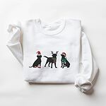 White crewneck sweatshirt laid flat with folded sleeves, embroidered with three black Labradors in a Santa hat and booties, reindeer antlers with a striped scarf, and a Santa hat with a green scarf