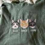 Green hoodie embroidered with three cat faces named Ollie, Dunkin and Sammy in white lettering
