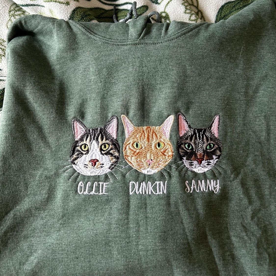 Three Cat Portrait Hoodie with Names Green hoodie embroidered with three cat faces named Ollie, Dunkin and Sammy in white lettering