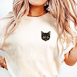 Woman with long wavy hair in an Ivory T-shirt embroidered with a small tortoiseshell cat face, black with golden caramel patches, on the left chest