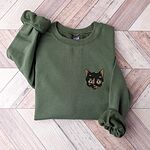 Military Green crewneck sweatshirt folded on a chevron wood floor with a tortoiseshell cat face, black with caramel patches, embroidered on the left chest