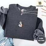 Dark Heather crewneck sweatshirt folded with ripped jeans and a silver chain necklace, embroidered with a white ghost hugging a black cat and carrying a jack-o'-lantern pail under bats, a crescent moon and stars