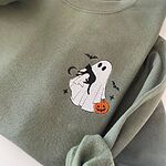 Military Green crewneck sweatshirt folded on a white table, embroidered on the left chest with a white ghost hugging a black cat and carrying a jack-o'-lantern pail under bats, a crescent moon and stars