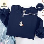 Navy crewneck sweatshirt folded with ripped jeans and a silver chain necklace, embroidered with a white ghost hugging a black cat and carrying a jack-o'-lantern pail under bats, a crescent moon and stars