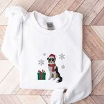 White crewneck sweatshirt laid flat on a herringbone wood floor, embroidered with a black tri Australian shepherd in a Santa hat and red scarf with a green gift box and silver snowflakes