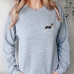 Woman in a Sport Grey crewneck sweatshirt embroidered with a black, tan and white corgi on the left chest