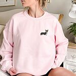 Woman sitting in a Light Pink crewneck sweatshirt embroidered with a small tricolor corgi with its ears up