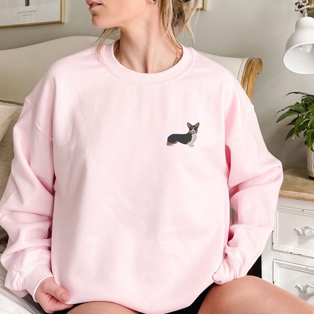 Tricolor Corgi Sweatshirt - worn in pink Woman sitting in a Light Pink crewneck sweatshirt embroidered with a small tricolor corgi with its ears up