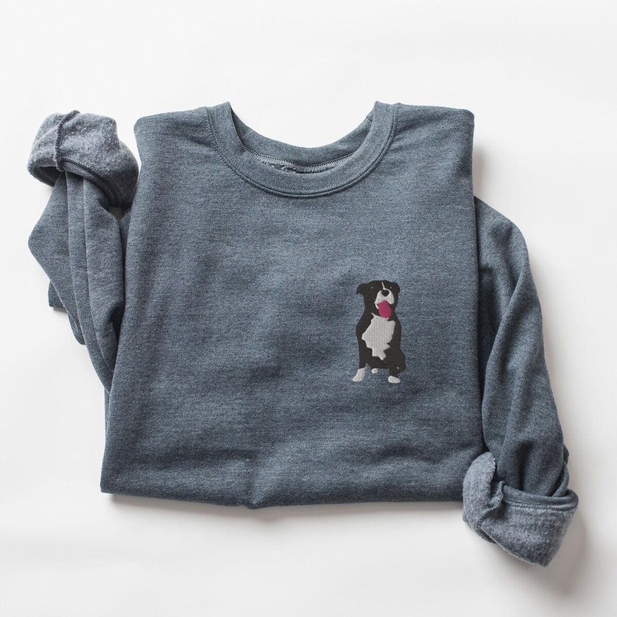 Tuxedo Pitbull Sweatshirt – Dark Heather Dark Heather crewneck sweatshirt laid flat with a rolled cuff, embroidered with a small black and white tuxedo pit bull sitting with its pink tongue out on the left chest