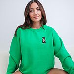 Woman sitting in an Irish Green crewneck sweatshirt embroidered with a small black and white tuxedo pit bull sitting with its pink tongue out on the left chest