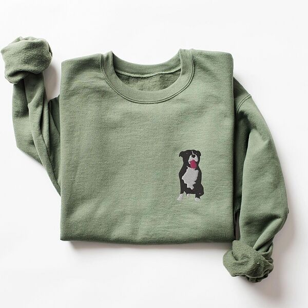 Military Green crewneck sweatshirt laid flat with a rolled cuff, embroidered with a small black and white tuxedo pit bull sitting with its pink tongue out on the left chest