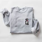 Sport Grey crewneck sweatshirt laid flat with a rolled cuff, embroidered with a small black and white tuxedo pit bull sitting with its pink tongue out on the left chest