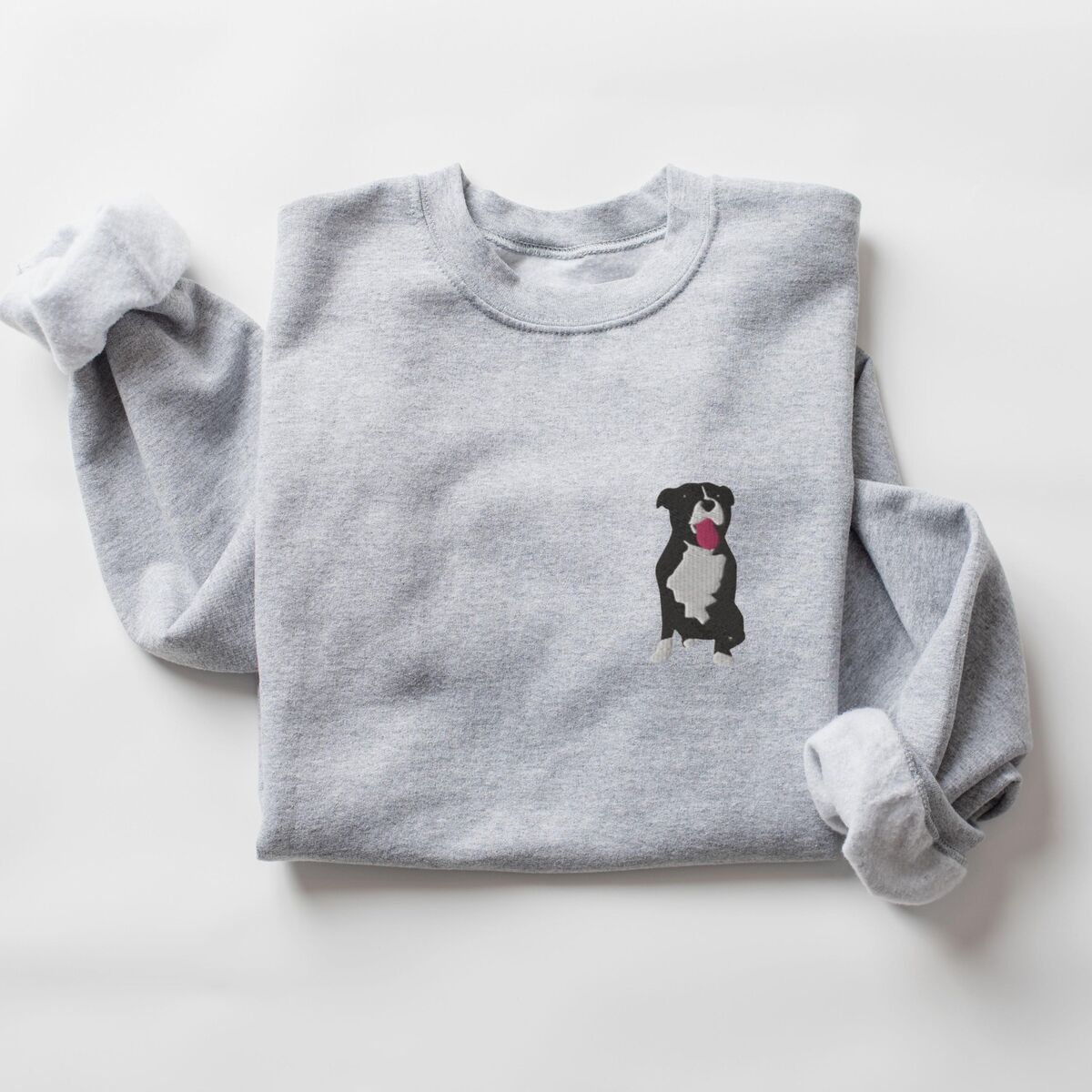 Tuxedo Pitbull Sweatshirt - Sport Grey Sport Grey crewneck sweatshirt laid flat with a rolled cuff, embroidered with a small black and white tuxedo pit bull sitting with its pink tongue out on the left chest