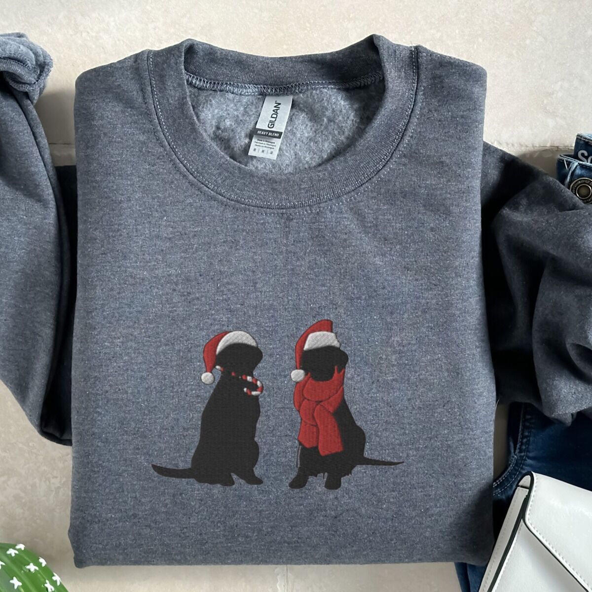 Two Black Labs Christmas Sweatshirt – Dark Heather Dark Heather crewneck sweatshirt laid flat on wood, embroidered with two black Labradors in Santa hats, one holding a candy cane and one in a red scarf