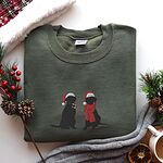Military Green crewneck sweatshirt folded with red berries, pine cones and a mug, embroidered with two black Labradors in Santa hats, one holding a candy cane and one in a red scarf