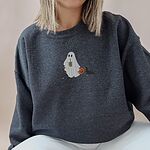 Woman sitting in a Dark Heather crewneck sweatshirt embroidered with a ghost sipping iced coffee between two black and tan dachshunds and a jack-o'-lantern pail