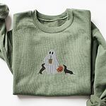 Military Green crewneck sweatshirt laid flat on white, embroidered with a ghost sipping iced coffee between two black and tan dachshunds and a jack-o'-lantern pail