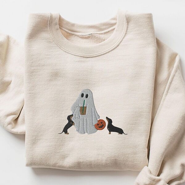 Sand crewneck sweatshirt laid flat on white, embroidered with a ghost sipping iced coffee between two black and tan dachshunds and a jack-o'-lantern pail