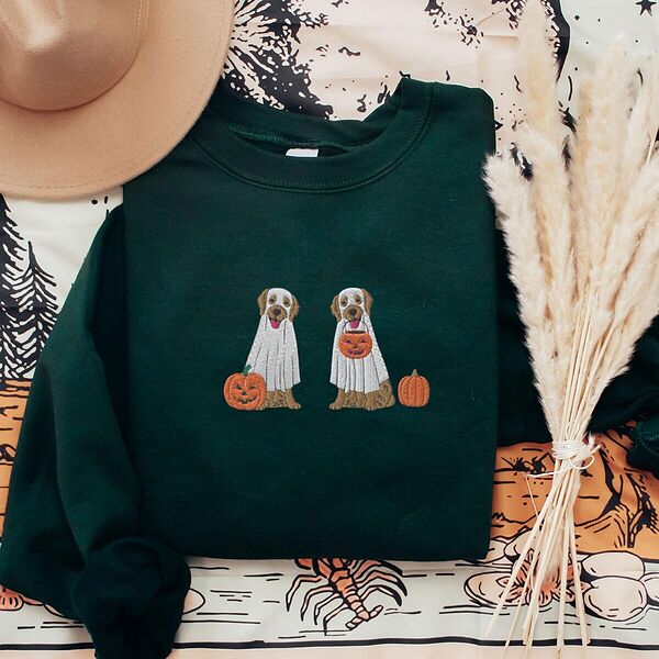 Forest Green crewneck sweatshirt laid flat with a brown hat and dried pampas, embroidered with two golden retrievers in white ghost sheets with a jack-o'-lantern, a pumpkin bucket and a small pumpkin