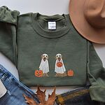Military Green crewneck sweatshirt laid flat with a brown hat, jeans and an autumn leaf, embroidered with two golden retrievers in white ghost sheets with a jack-o'-lantern, a pumpkin bucket and a small pumpkin