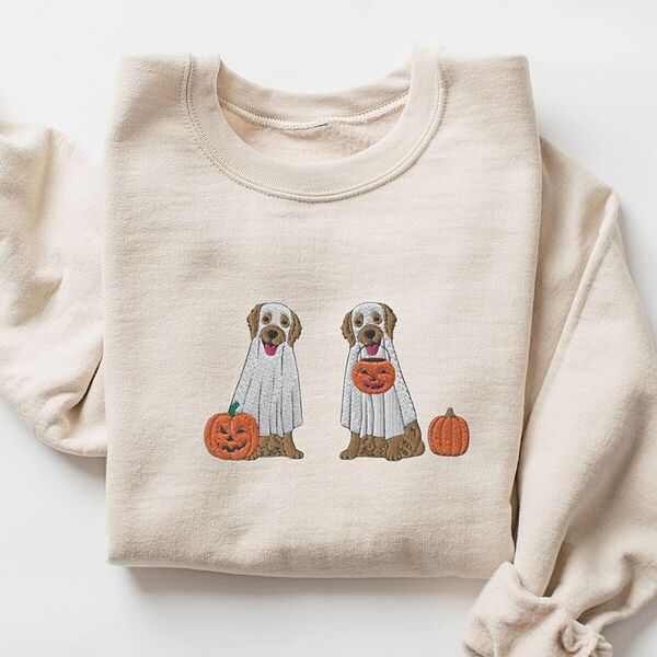 Sand crewneck sweatshirt laid flat with a rolled sleeve, embroidered with two golden retrievers in white ghost sheets with a jack-o'-lantern, a pumpkin bucket and a small pumpkin