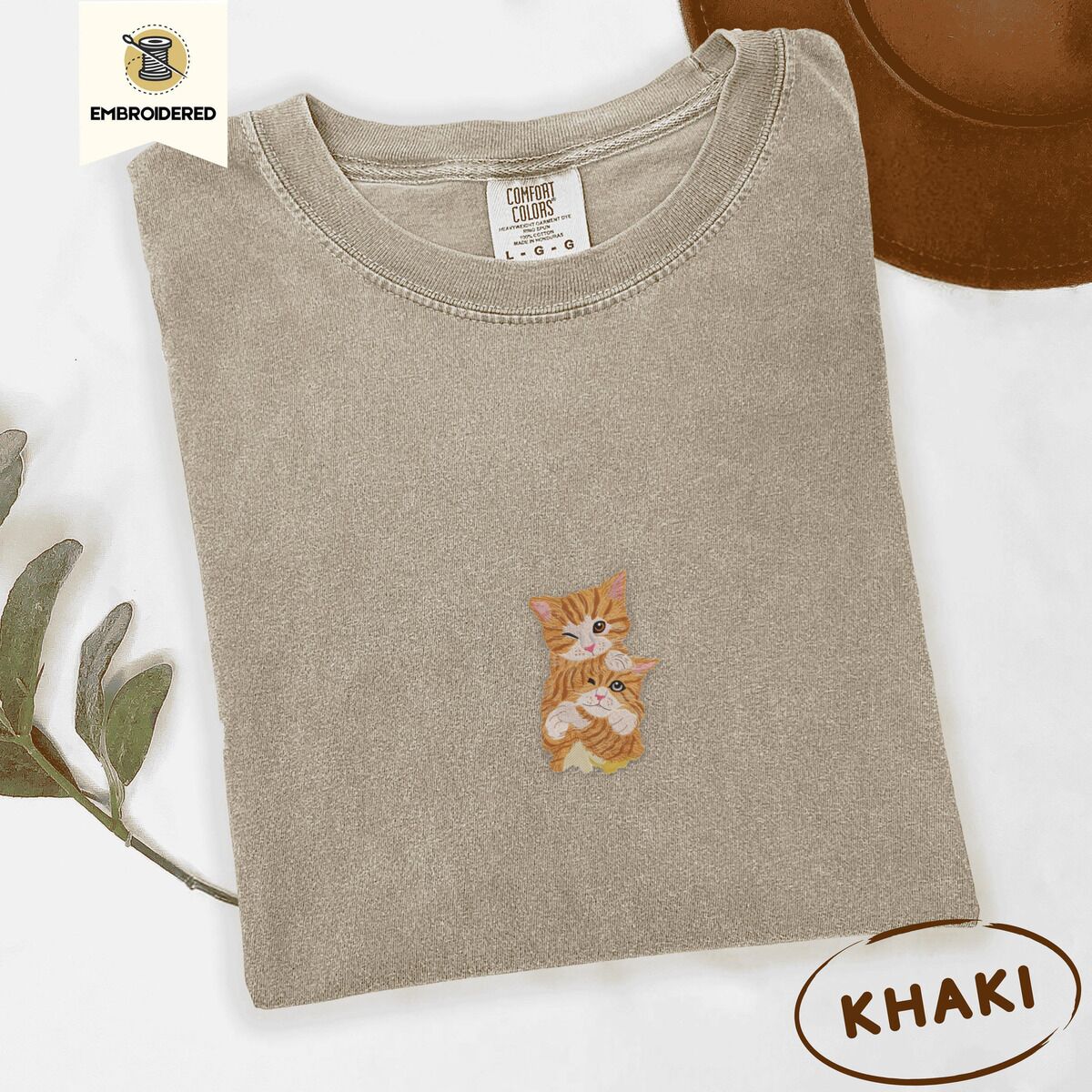 Two Kittens Shirt – Khaki Khaki Comfort Colors T-shirt embroidered with two orange tabby kittens, one winking with a paw on the other's head