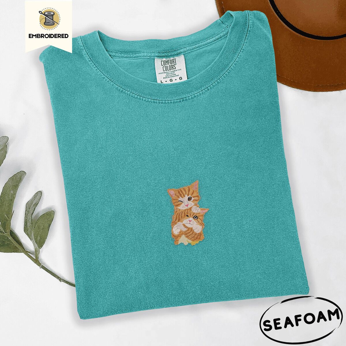 Two Kittens Shirt – Seafoam Seafoam Comfort Colors T-shirt embroidered with two orange tabby kittens, one winking with a paw on the other's head