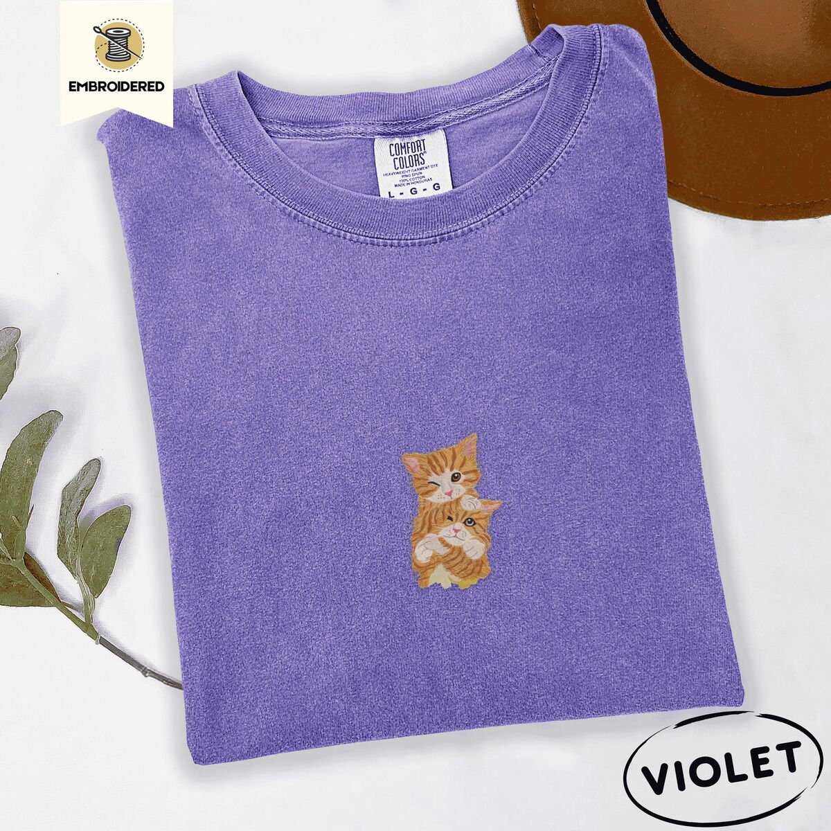 Two Kittens Shirt – Violet Violet Comfort Colors T-shirt embroidered with two orange tabby kittens, one winking with a paw on the other's head