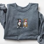 Dark Heather crewneck sweatshirt laid flat, embroidered with a black and white tuxedo pit bull and a fawn pit bull sitting side by side with their tongues out, centered on the chest