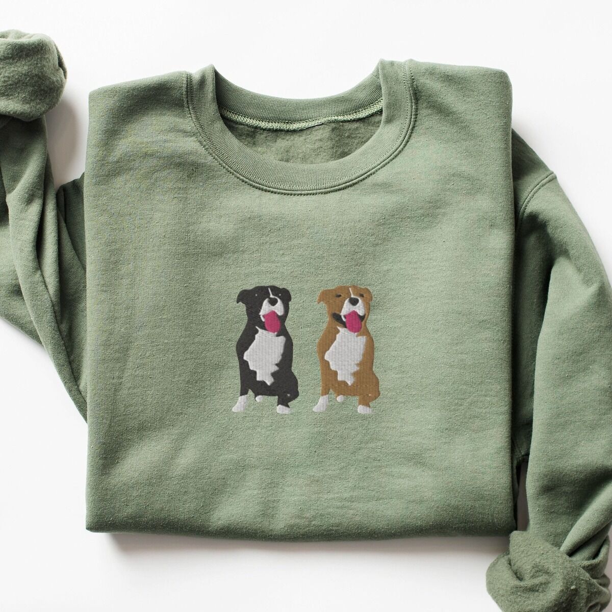 Two Pitbulls Sweatshirt – Military Green Military Green crewneck sweatshirt laid flat, embroidered with a black and white tuxedo pit bull and a fawn pit bull sitting side by side with their tongues out, centered on the chest