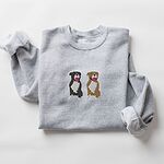 Sport Grey crewneck sweatshirt laid flat with a rolled cuff, embroidered with a black and white tuxedo pit bull and a fawn pit bull sitting side by side with their tongues out, centered on the chest