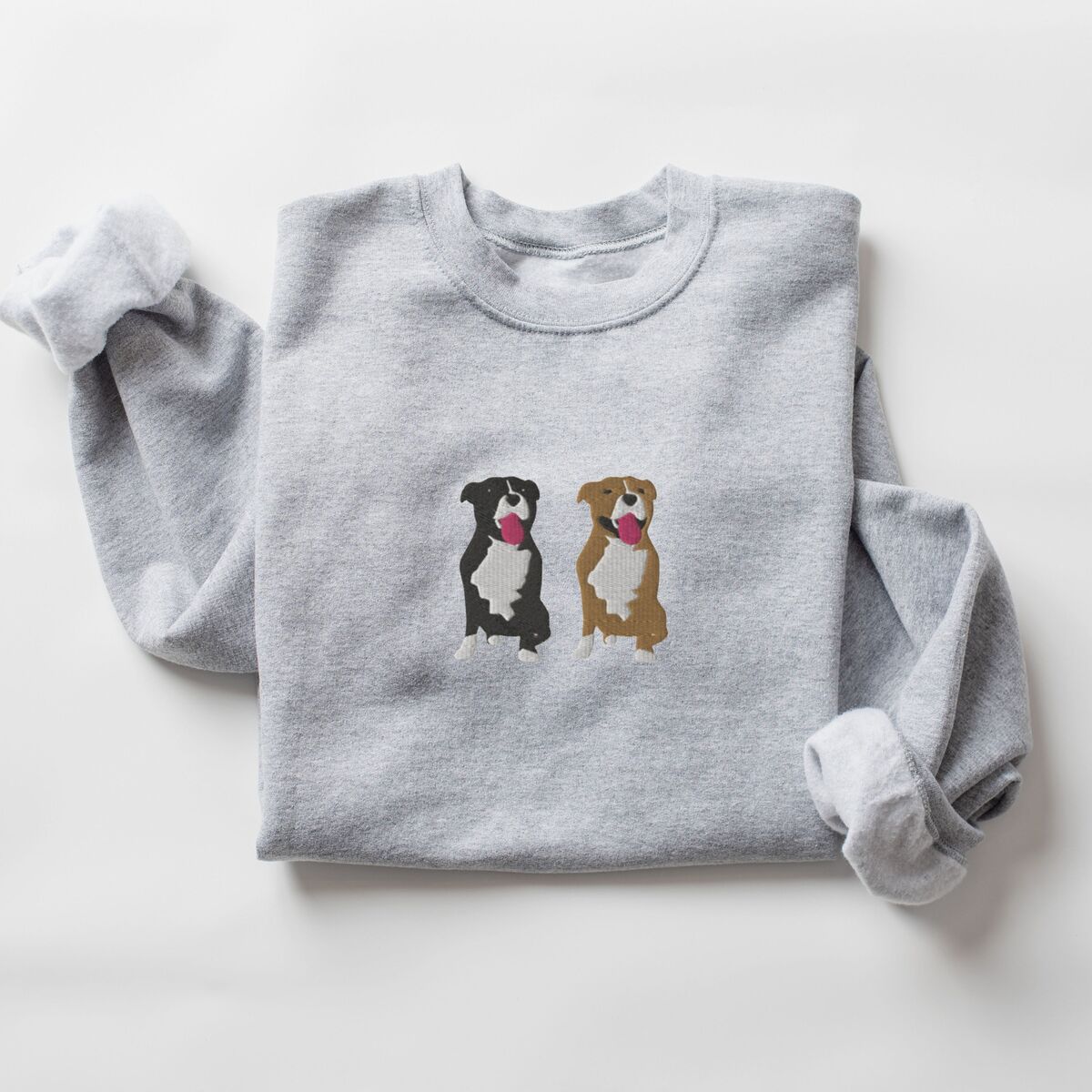 Two Pitbulls Sweatshirt - Sport Grey Sport Grey crewneck sweatshirt laid flat with a rolled cuff, embroidered with a black and white tuxedo pit bull and a fawn pit bull sitting side by side with their tongues out, centered on the chest